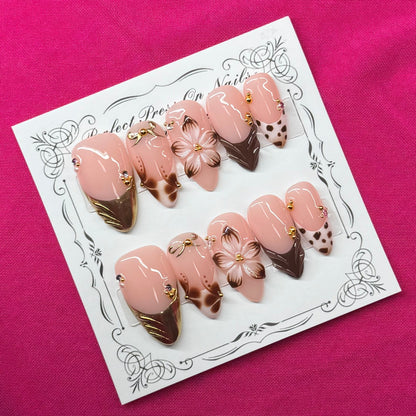 A set of 10 false press-on nails displayed on a white decorative card, featuring a pink and white ice cream cone design with chocolate drizzle and white chocolate flowers, set against a bright pink fabric background.